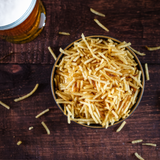 A birds eye view of a bowl of chicken salt fries on a wooden table next to a pint of beer.