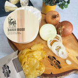 An open 40g pack of Made For Drink's Baron Bigod Cheese & Onion potato crisps lying on a wooden board with slices of white onion and a pack of Baron Bigod brie-style cheese.