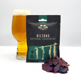 A 30g pack of Made For Drink's 100% Irish Grass-Fed Beef Biltong standing in front of a pint of lager with a small pile of biltong in the foreground.