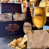An open 40g pack of Made For Drink's Baron Bigod Cheese & Onion potato crisps lying in front of a bottle and glass of Aspall draught cyder and a box of 4 packs of crisps.