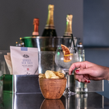 A sliver box holding 40g packs of Made For Drink's award-winning Dorset Sea Salt flavoured English Heritage potato crisps. A bowl of crisps in the foreground with a hand reaching to take one.
