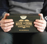 A man holding a Made For Drink gift box on his lap wit two hands.