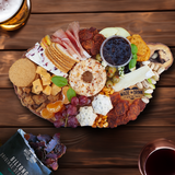 A Made for Drink charcuterie board with chorizo thins, cheese, crackers nuts, olives and fruits. In the corners a pink of beer and glass of red wine are just visible, along with an open packet of our Beef Biltong.